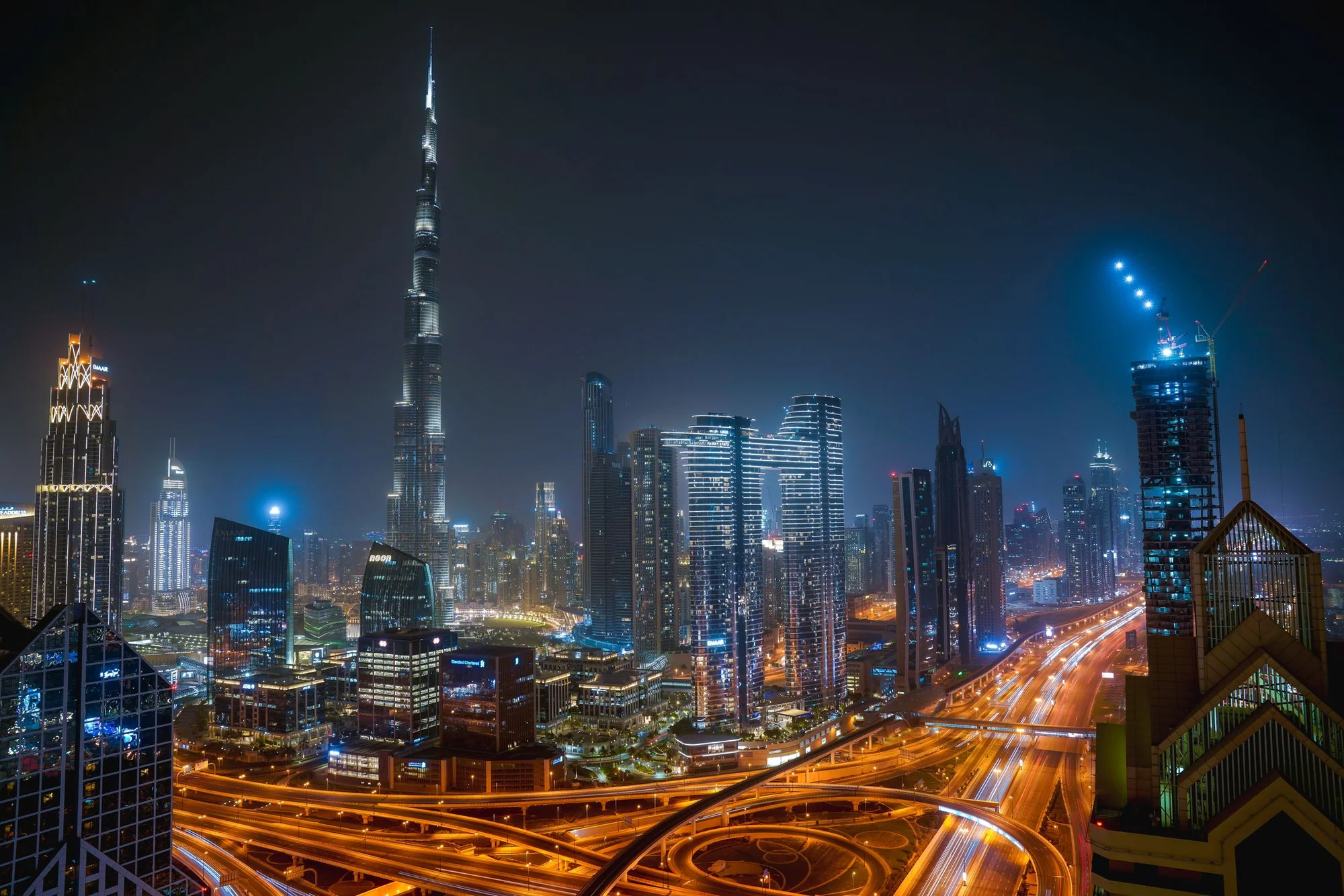 Photograph of Downtown Dubai and the Burj Khalifa at night, with illuminated roads and office towers.